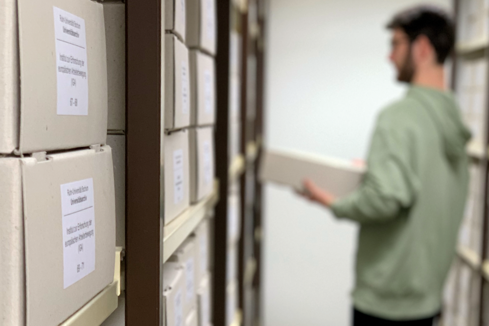 Ein Mitarbeiter des Universitätsarchivs stellt einen Archivkarton in einem Magazinraum in das entsprechende Regalfach