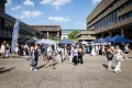 Photo: Stands and visitors in sunny weather at the Nordforum of Ruhr University Bochum