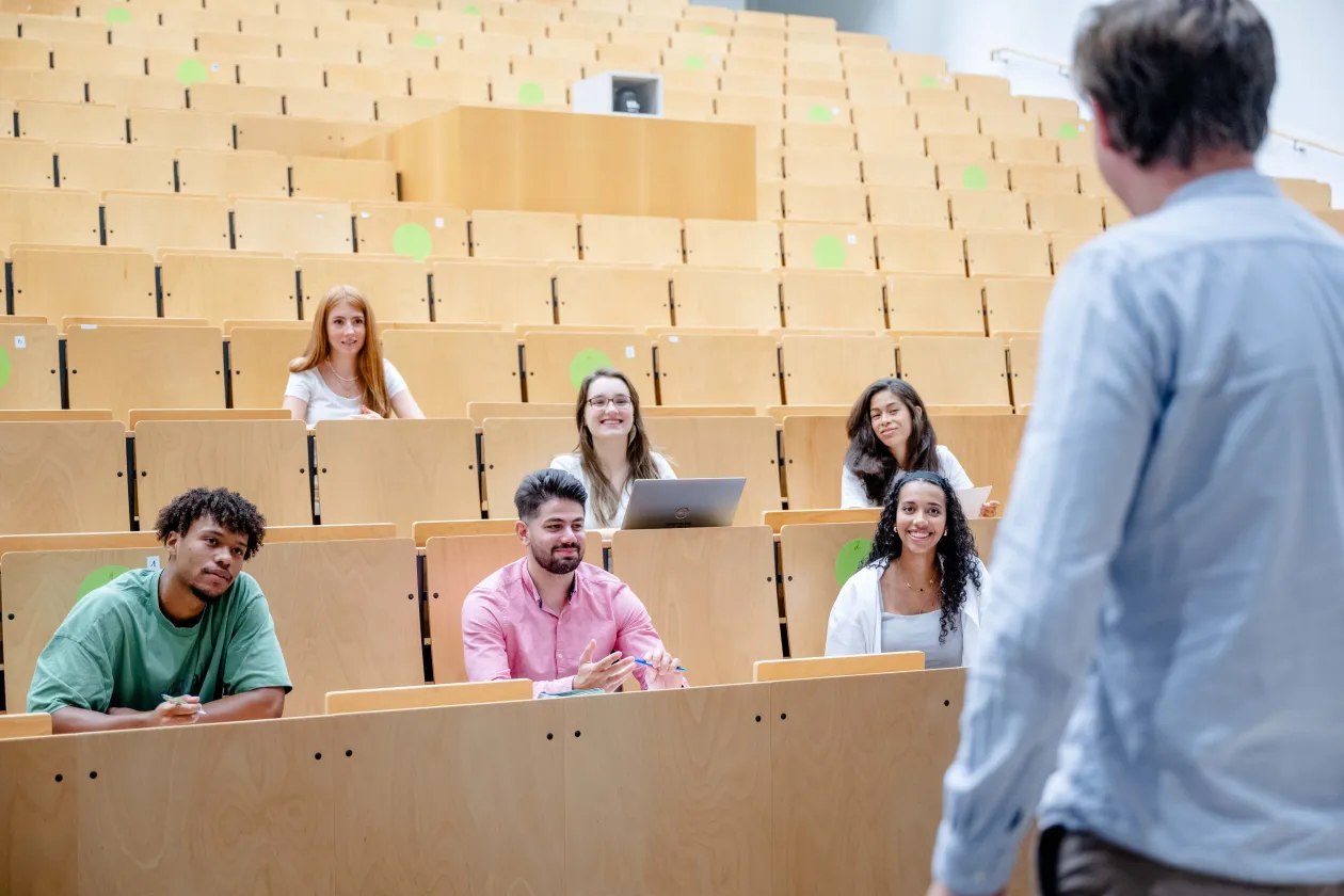 Studierende sitzen in einem Hörsaal und schauen den Dozenten an.
