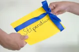 Hände die einen Umschlag mit der Aufschrift "Stipendium" übergeben.