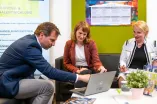 Drei Personen in einer Sitzgruppe schauen und zeigen auf den Laptop-Bildschirm.