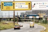 Die Farbfotografie zeigt eine Ansicht der Universitätsstraße in Richtung Langendreer/Witten in den 1970er Jahren. Links neben der Straße sind die Straßenbahngleise zu sehen. Im Hintergrund von links nach rechts befinden sich die Unibrücke, die im Bau befindlichen Werkhallen vor der I-Gebäudereihe.