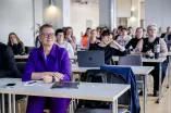 Foto: Teilnehmende einer Veranstaltung in Sitzreihen mit Tischen.