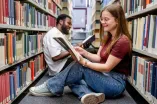 Zwei Studierende sitzen in der Bibliothek auf dem Boden und lesen
