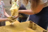 Junge Frau füllt Lehm in Hände von Mädchen über einem Tisch.