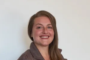 Nina Bartholomé lächelt im Halbprofil in die Kamera, trägt einen braunen Blazer