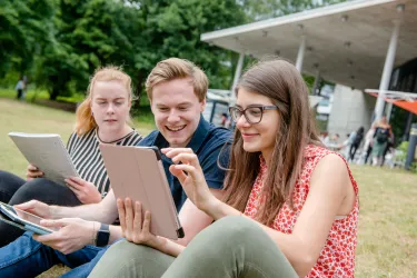 Studierende auf der Wiese vor dem Q-West mit Tablet