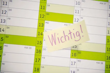 Hand klebt Post-it mit Aufschrift Wichtig auf einen Kalender.