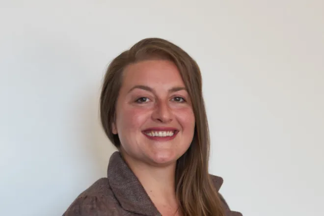 Nina Bartholomé lächelt im Halbprofil in die Kamera, trägt einen braunen Blazer