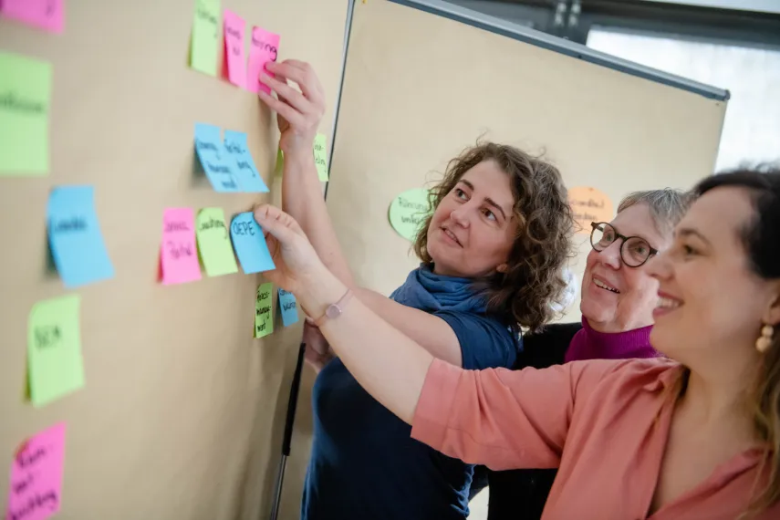 Kolleginnen des OEPE-TEams strukturieren Beiträge an der Pinnwand.