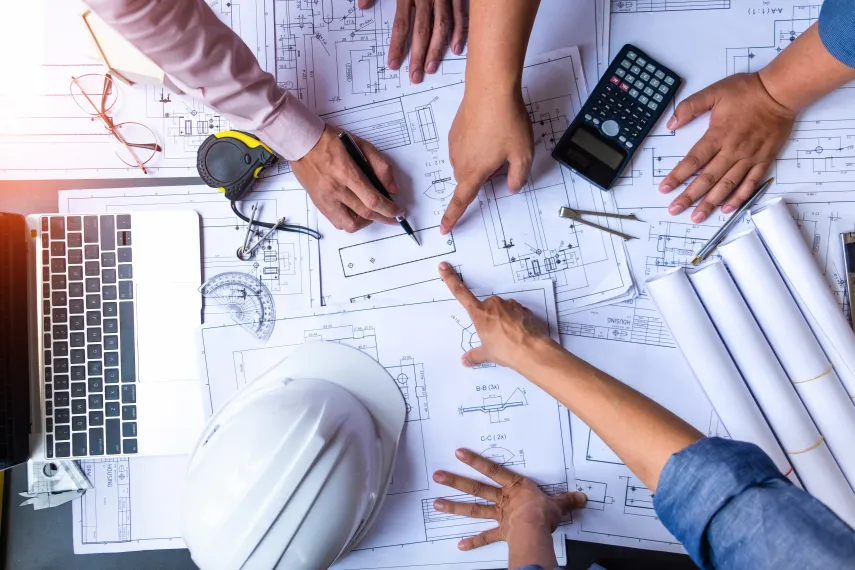 Ingenieure zeigen im Büro auf das Bau-Konzept und zeichnen mithilfe des Laptops das Design des Gebäudeprojekts. 