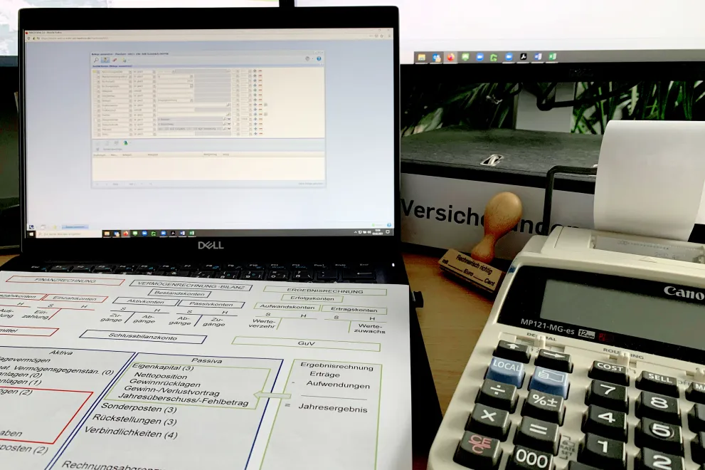 Mappe, PC, Rechenmaschine, Stempel und ein Dokument auf dem Schreibtisch ausgebreitet. 