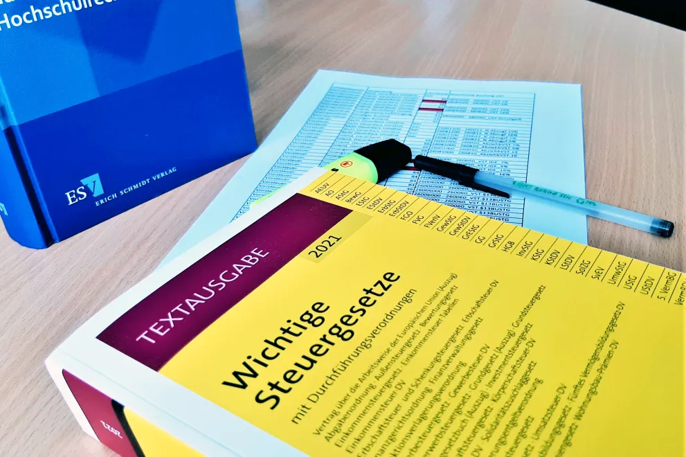 Bücher Steuergesetze und Hochschulrechnungslegung liegen neben Formular und Kulli auf einem Tisch. 