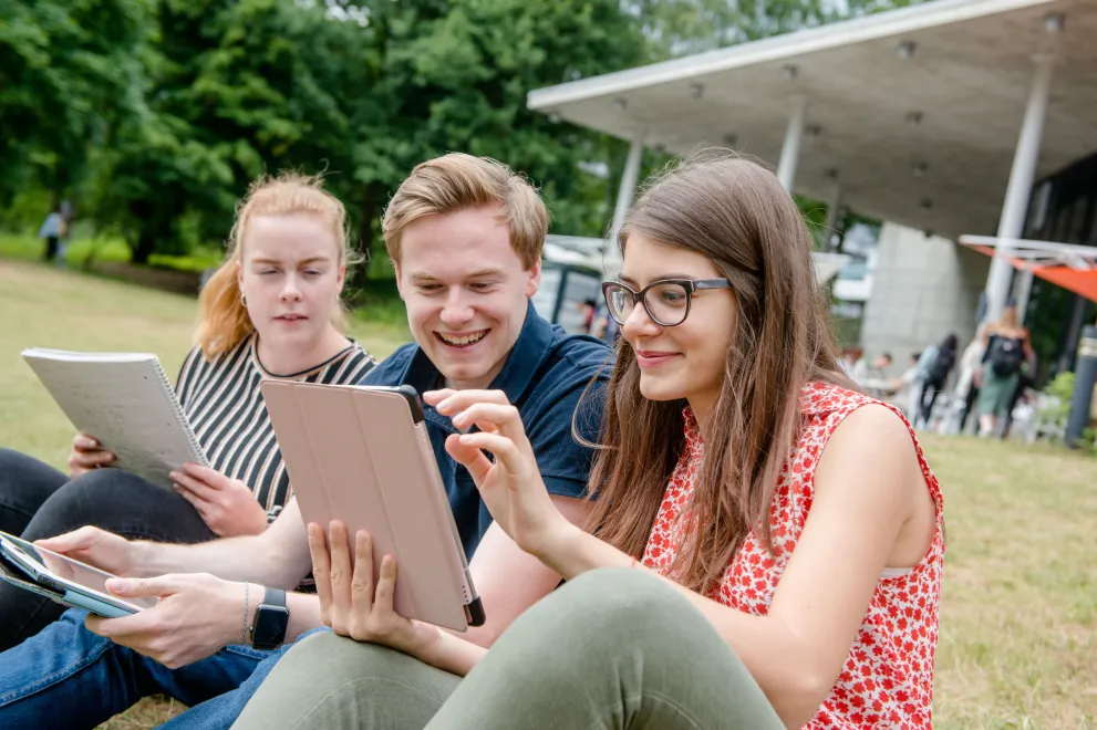 Studierende auf der Wiese vor dem Q-West mit Tablet