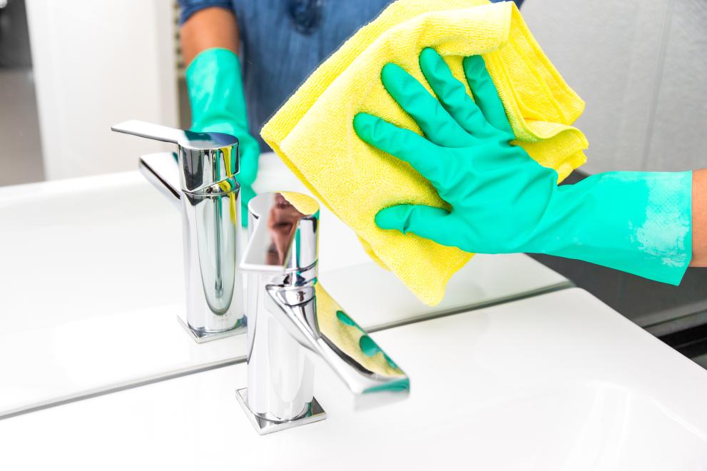 Eine Reinigungskraft sorgt mit Putzlappen für Hygiene und Sauberkeit im Bad.