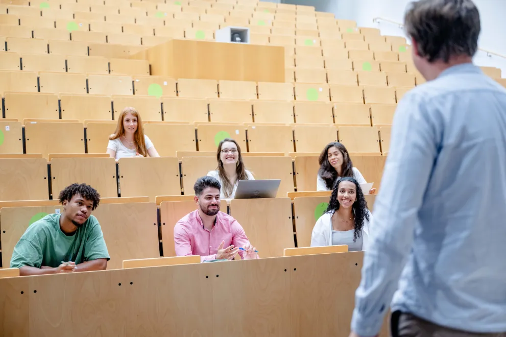 Studierende sitzen in einem Hörsaal und schauen den Dozenten an.