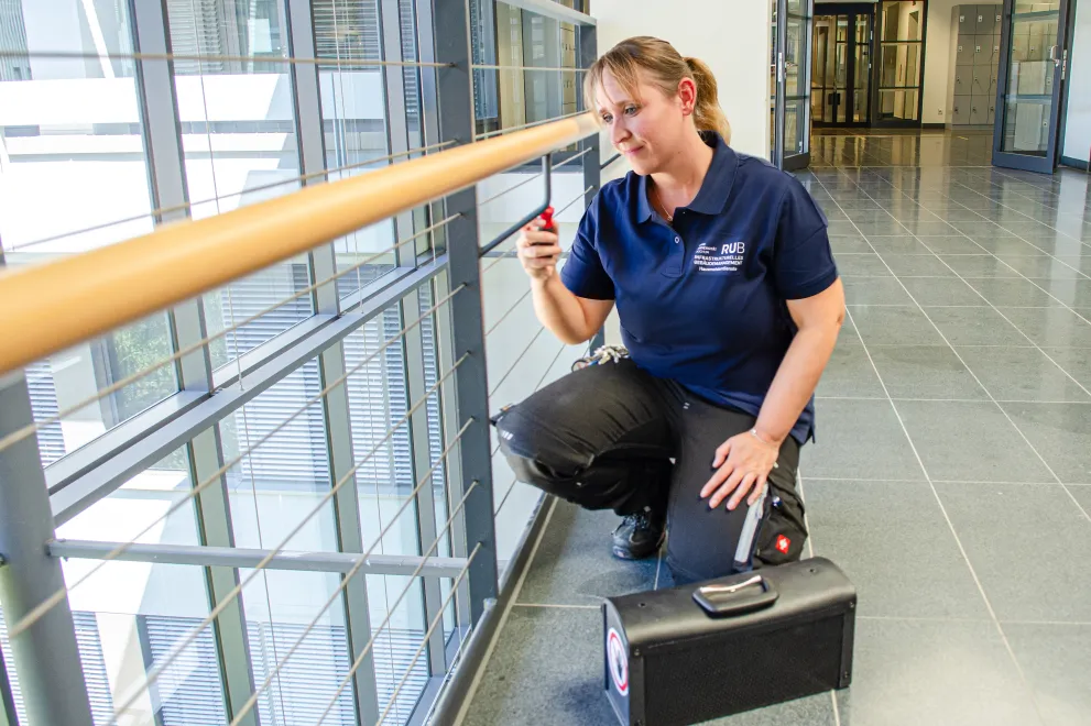 Eine Mitarbeiterin der Hausmeisterdienste der RUB schraubt im Gebäude Geländer fest.