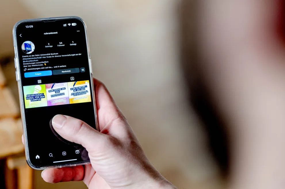 POerson schaut auf ein Handy, auf dem der Instagram-Eventkanal der RUB aufgerufen ist.
