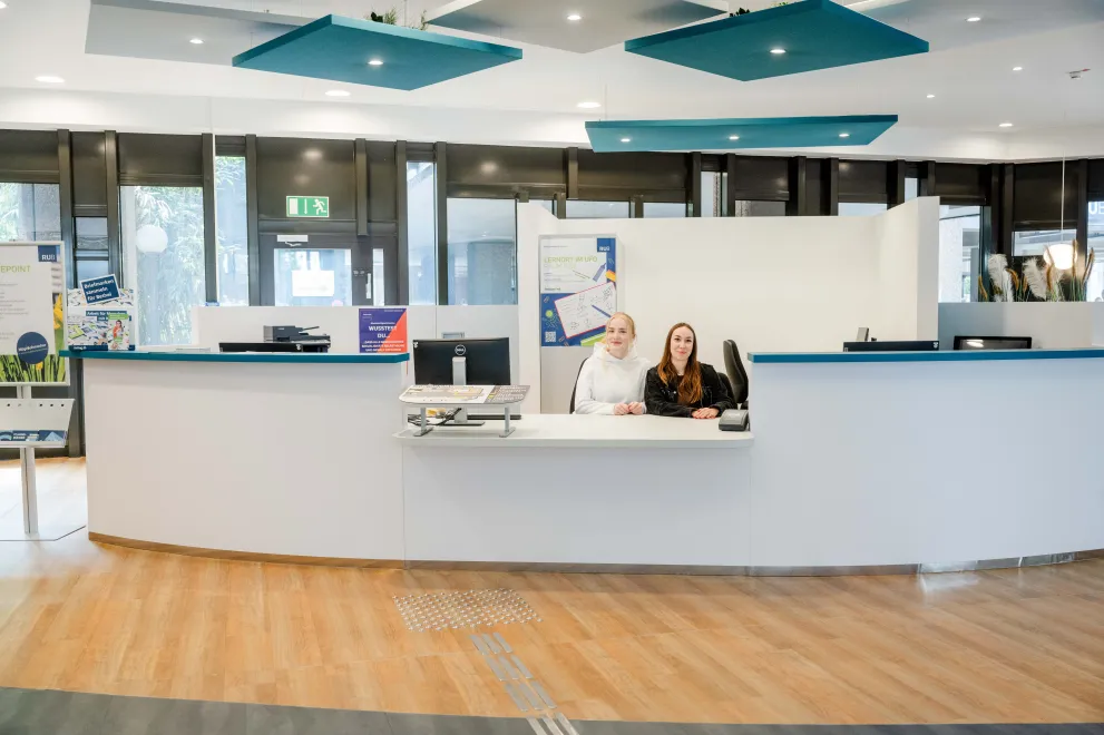 Photo: Two people sitting behind a white counter.