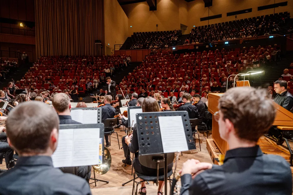 Photo: Orchestra plays in the large hall of the Audimax, which is full to capacity.