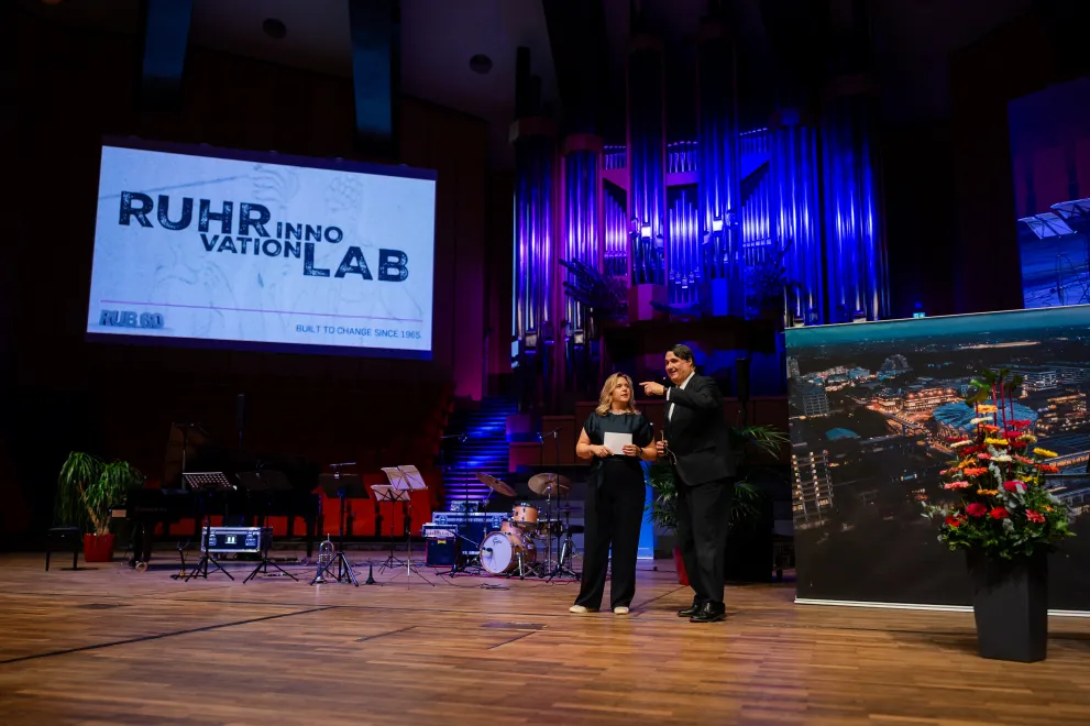 Foto: Akademische Jahresfeier 2025 im Audimax, Moderatorin Henrike Tönnes und Rektor Prof. Dr. Martin Paul auf der Bühne