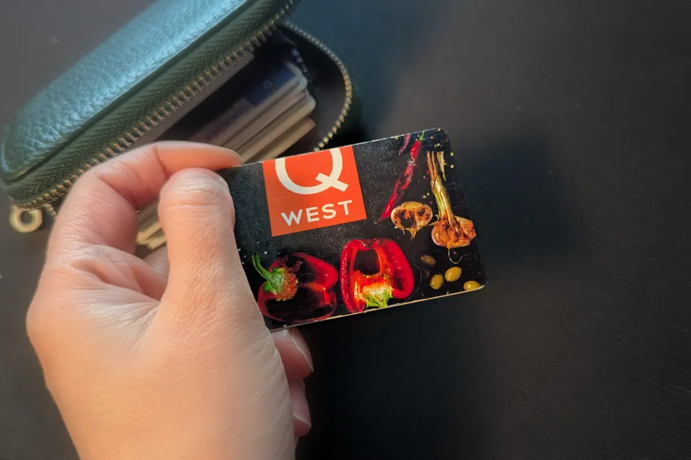 Das Bild zeigt eine Hand, die eine Q-West Karte hält, im Hintergrund ein Portemonaie.