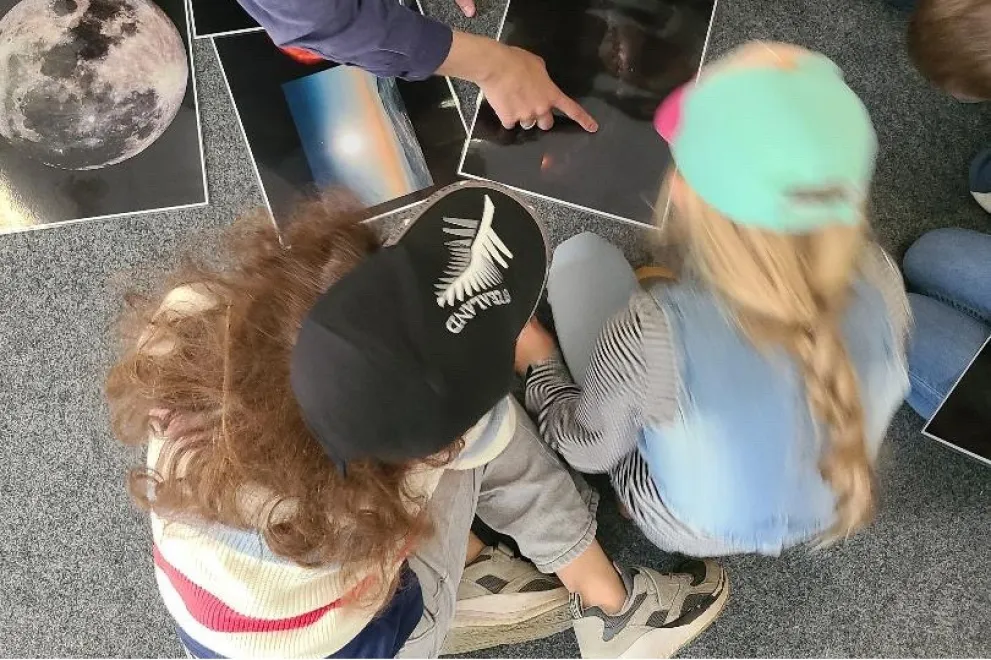 Kinder der Osterfreizeit bekommen astronomische Bilder vom Doktorand des Astronomischen Institutes auf dem Boden sitzend erklärt.