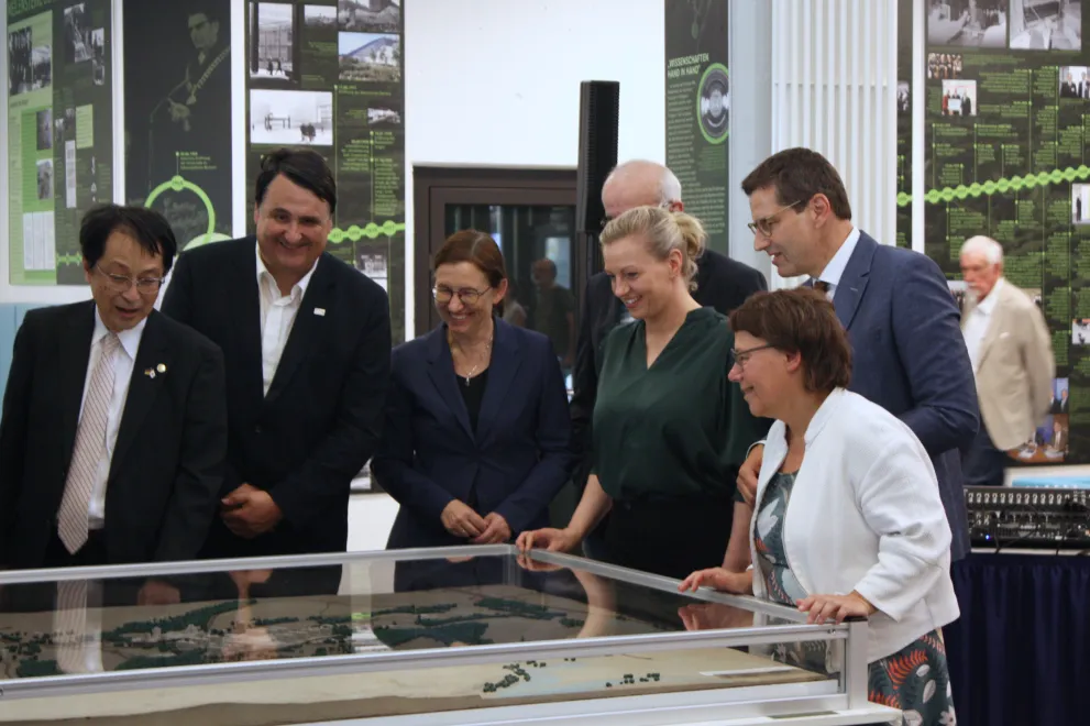Fotodokumentation der Ausstellungseröffnung. An zentraler Stelle ist das Architekturmodell der Universität zu sehen, umgeben von den Rektor*innen der UA Ruhr, Kanzlerin, Leitung des Universitätsarchivs, OB der Stadt Bochum sowie weiteren Gästen