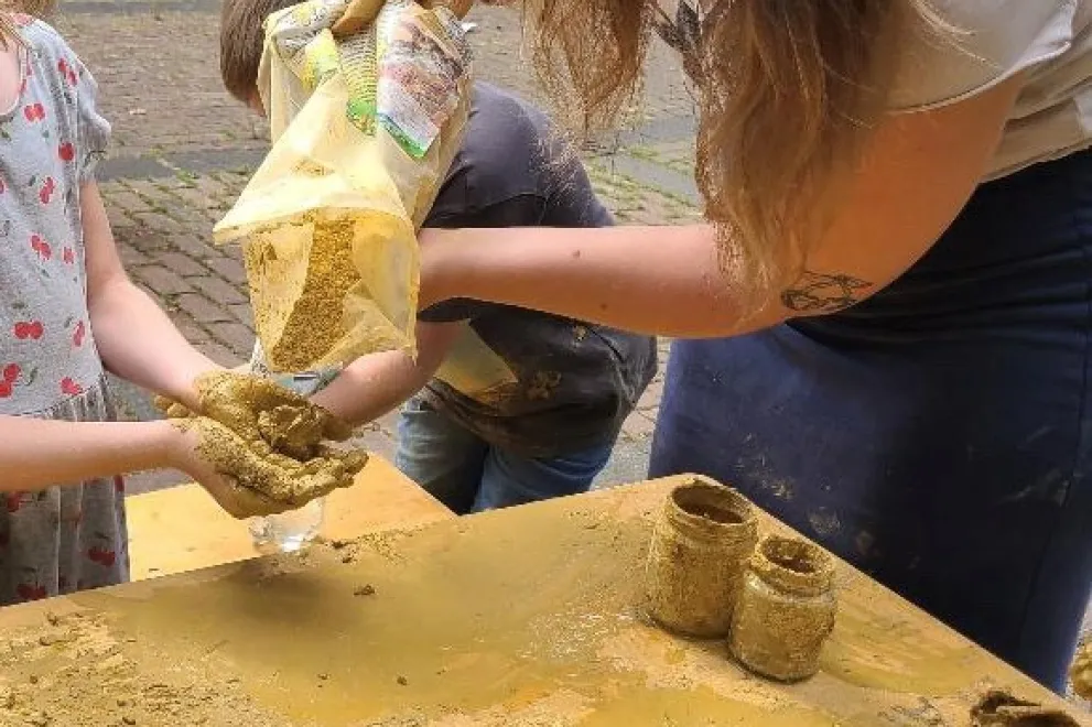 Junge Frau füllt Lehm in Hände von Mädchen über einem Tisch.