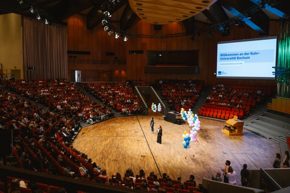 Welcome event for first-year students in the Audimax: View from the seating rows toward the stage, a side screen, and the seating rows across from them