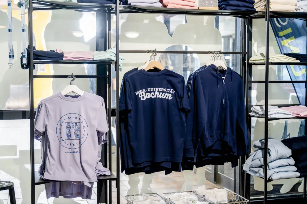 Das Foto zeigt mehrere aufgehängte Shirts und Sweatshirts im Unishop auf dem RUB-Campus