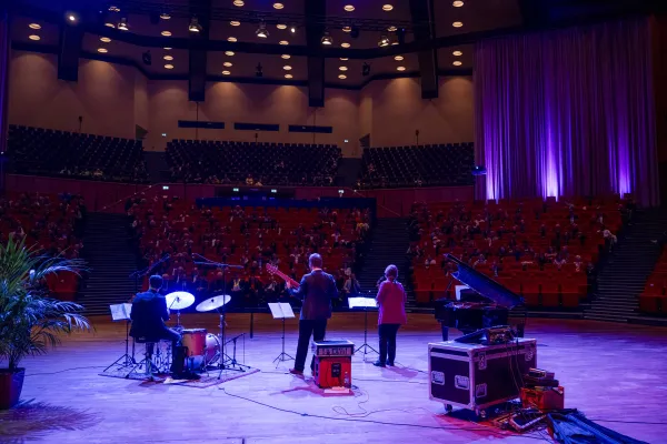 Foto: Band vor den Sitzreihen im Audimax. Der Saal ist abgedunkelt.