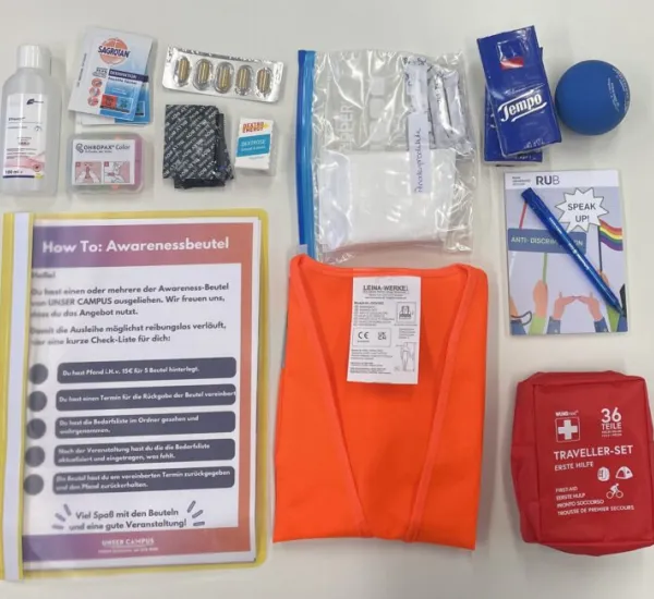 Awareness-Beutel Verschiedene Materialen liegen auf einem weißen Hintergrund. Zu sehen sind eine Mappe, eine Warnweste, eine Erste-Hilfe-Tasche, Hygiene- und Schreibutensilien.